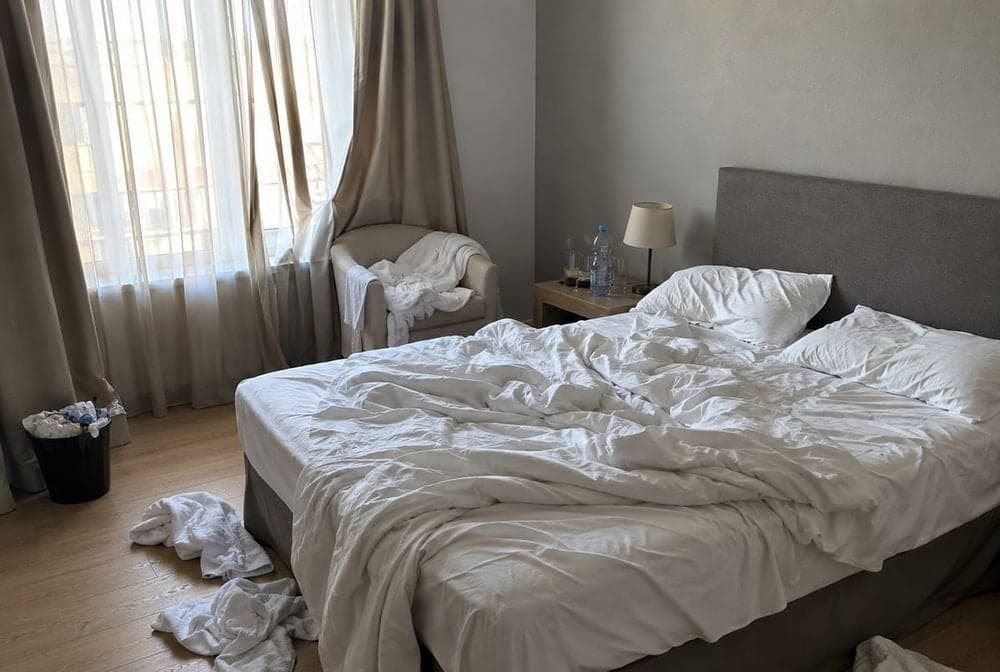 La même chambre avec lit défait, linge et affaires au sol